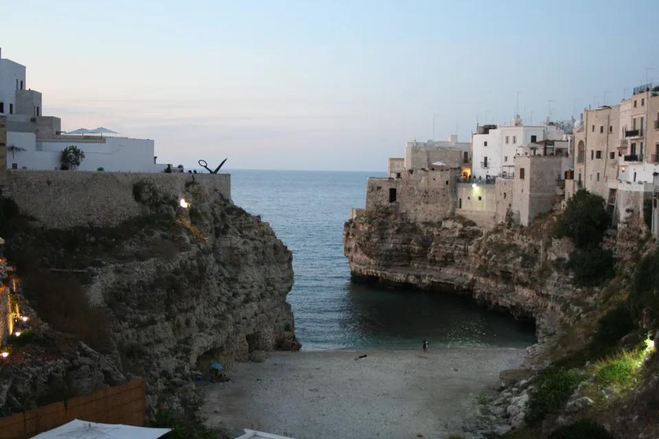 The pebble cove of Lama Monachile at Polignano a Mare seen at dusk from the Ponte Borbonico, wedged between two limestone cliffs with the old town above